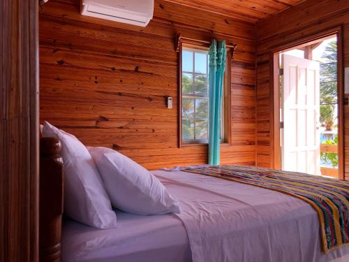 a bedroom with a bed with wooden walls and a window at Blue Wave Guest House in Caye Caulker
