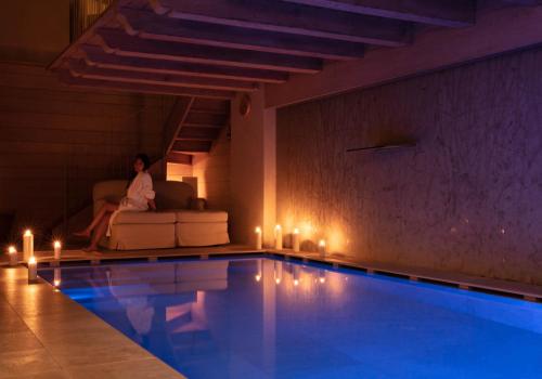 a woman sitting on a couch next to a swimming pool at Auberge de La Maison in Courmayeur