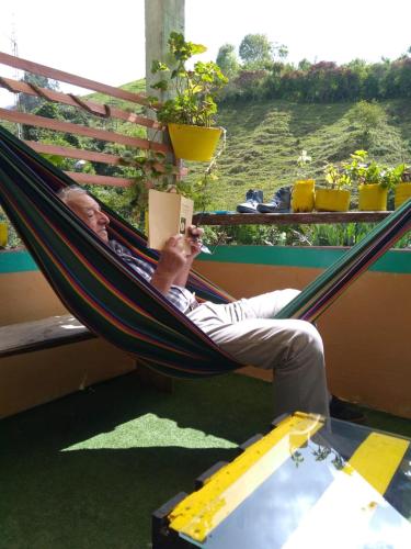 a man sitting in a hammock reading a book at HOSTAL CASA VICTORIA PIJAO in Pijao