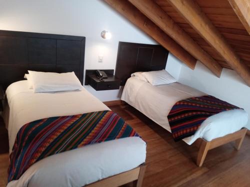 two beds in a room with wooden ceilings at Yanapanakusun Cusco in Cusco