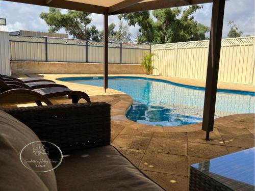 una piscina con sillas y sombrilla en Seashells Holiday House - Kalbarri, en Kalbarri