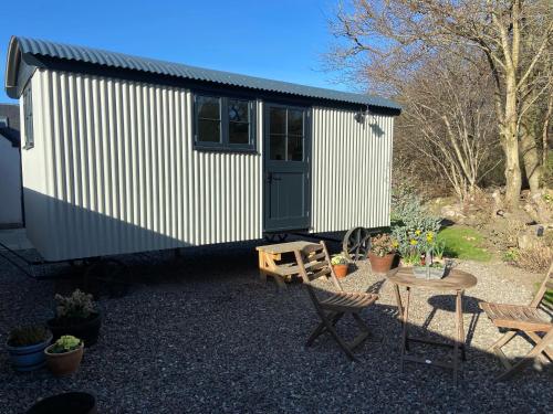 a small white shed with a table and chairs at Peaceful Shepherd’s Hut in beautiful countryside. in Linlithgow