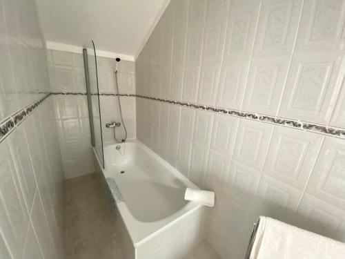 La salle de bains blanche est pourvue d'une douche et d'une baignoire. dans l'établissement Ericeira Sand Beach F7, à Ericeira