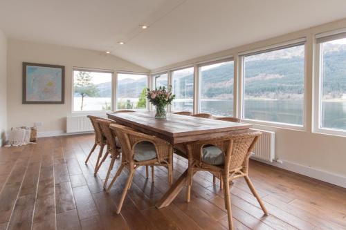 a dining room with a table and chairs and windows at Rossmay House - 4 Bedroom Scottish Villa with waterfront / mountain views in Arrochar