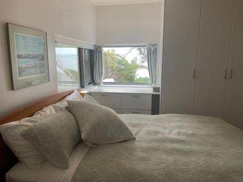 ein Schlafzimmer mit einem Bett mit Kissen und einem Fenster in der Unterkunft Beachside Taroona with Spa in Sandy Bay