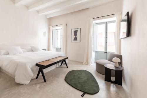 a white bedroom with a large bed and a chair at Meem Townhouse in Sóller