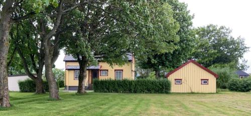 una pequeña casa amarilla en un patio con árboles en Sjarmerende hus med veldig stort uteareal. en Brekstad