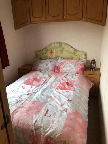 Una cama con un edredón rosa y blanco. en Lovely 3 bedroom 8 berth caravan in Rhyl, en Rhyl