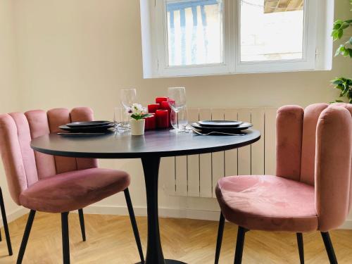 una mesa con sillas rosas y una mesa con platos y vasos. en La Roseraie, en Rouen