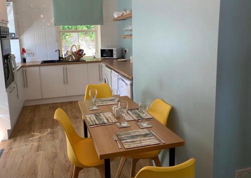 uma cozinha com uma mesa de madeira e cadeiras amarelas em Seaview Cottage em Ascog