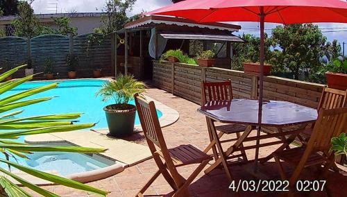 a table and chairs with an umbrella next to a pool at Agréable chambre d'hôtes, SDB, piscine, carbet cuisine. in Saint-Claude