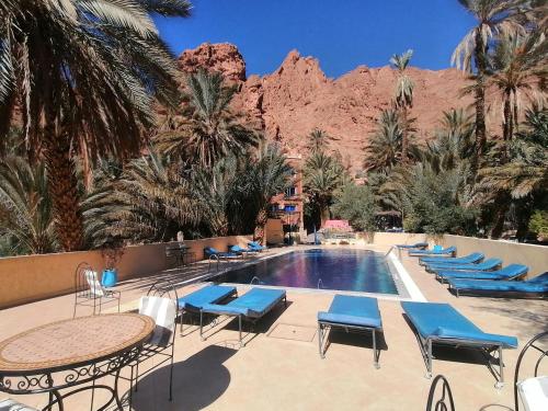 a resort with a pool with palm trees and a mountain at Auberge Camping Atlas in Tinerhir