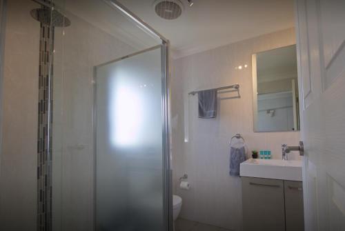 a bathroom with a shower, sink, and mirror at Tuncurry Motor Lodge in Tuncurry