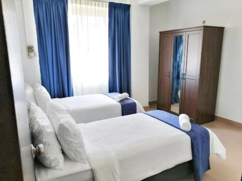 two beds in a hotel room with blue curtains at FAMISA Eastern Gold Service Apartment in Kertih