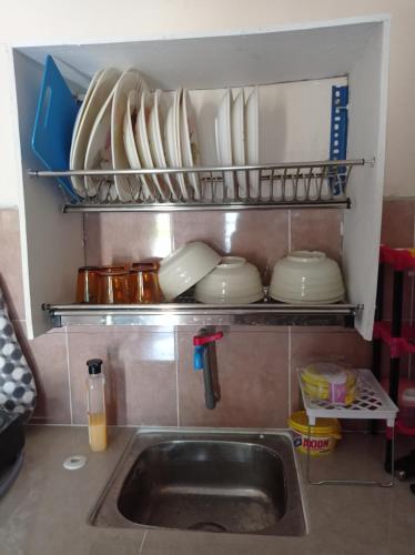 um lavatório de cozinha com pratos e pratos numa prateleira em Bonda Guesthouse III em Paka