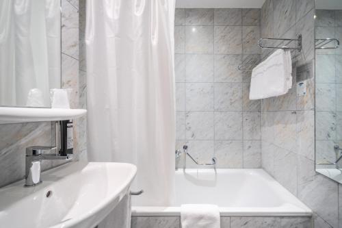 a white bathroom with a tub and a sink at The Guesthouse by The Hey Hotel in Interlaken