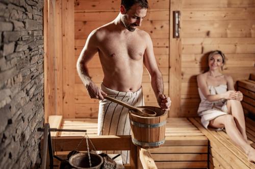 a man stirring a pot in a sauna with a woman at Panoramahotel Huberhof in Maranza