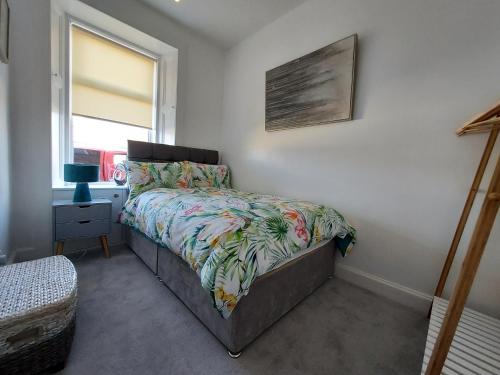 a bedroom with a bed with a floral bedspread and a window at Duke Street Apartment in Lilliesleaf