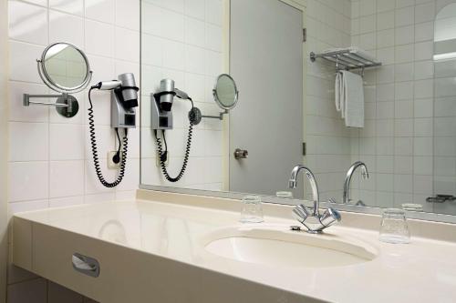 a bathroom with a sink and two phones on a mirror at NH Capelle Rotterdam in Capelle aan den IJssel