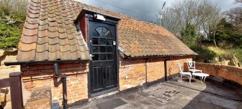 a small brick building with a black door and a chair at 17th-Century1Bed Studio PetsOk Garden Wifi in Elkesley