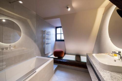 a bathroom with a tub and a sink and a mirror at Hotel Le Colombier in Colmar
