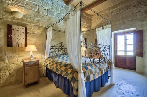 a bedroom with a canopy bed in a stone wall at Farmhouse Razzett Cora in Victoria