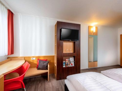 a hotel room with a bed and a desk and a tv at ibis Kassel Melsungen in Melsungen