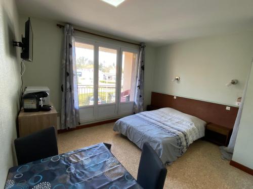 a bedroom with a bed and a table and a window at Les studios meublés de la résidence Beatrice in Bourbonne-les-Bains