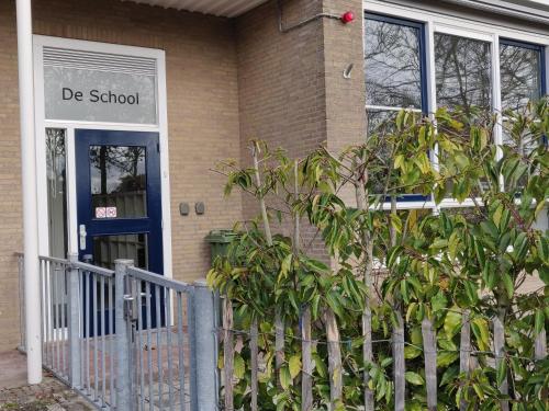a school building with a blue door and a fence at LOGEMENT DE SCHOOL Middelburg in Middelburg