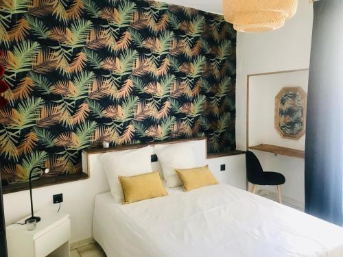 a bedroom with a white bed with a tropical wallpaper at Appartement Lavande et Jasmin in Anduze