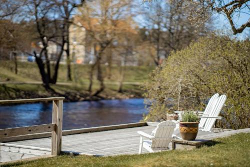 two white chairs sitting on a wooden deck next to a river at Hotell Villa Rönne in Ängelholm