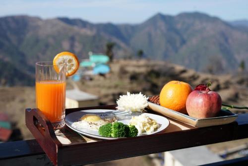 a table with a plate of food and a glass of orange juice at Hotel Alpine Musk in Kanatal