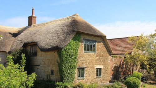 an old stone house with a thatched roof at Courtyard Cottage at Stepps House in Ilminster