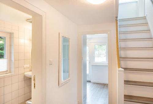 a bathroom with white walls and a mirror and stairs at Das kleine Haus - Reetdachhaus Petersen in Nebel