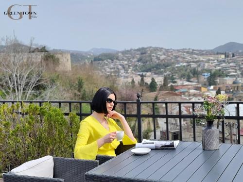 a woman sitting at a table with a cup of coffee at Hotel Green Town in Kutaisi