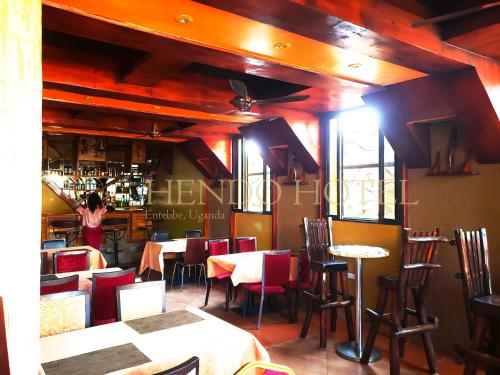 a restaurant with tables and chairs and a woman standing in a bar at Hendo Hotel in Entebbe