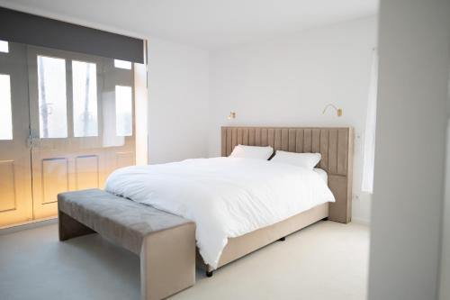 a white bedroom with a large bed and a bench at La Rose du Cèdre in Gray