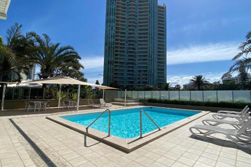 a swimming pool with chairs and a tall building at Hi Surf Beachfront Resort Apartments OFFICIAL SITE in Gold Coast