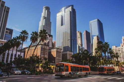 deux bus dans une rue urbaine avec de grands bâtiments dans l'établissement Pineapple Hostel, à Los Angeles