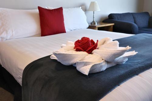 Una cama blanca con una rosa roja. en Baywatch Motor Lodge, en Timaru