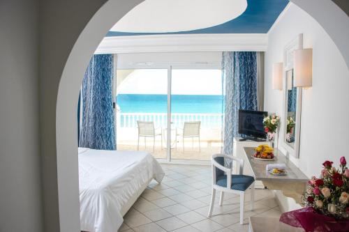 a hotel room with a bed and a desk with a view of the ocean at Cap Bon Kelibia Beach Hotel & Spa in Kelibia
