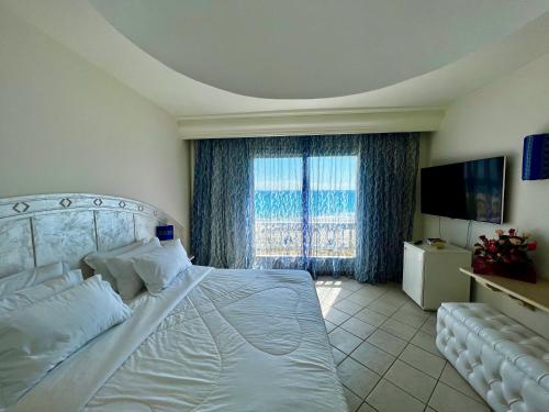 a bedroom with a white bed and a large window at Cap Bon Kelibia Beach Hotel & Spa in Kelibia