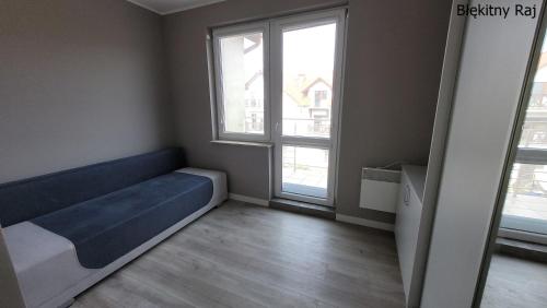 um quarto com um sofá azul e duas janelas em Apartament Błękitny Raj em Krynica Morska