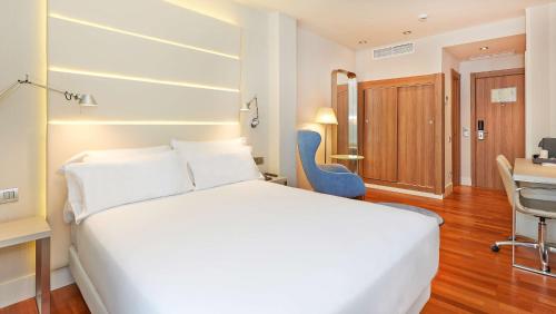 a bedroom with a large white bed and a blue chair at NH Barcelona Les Corts in Barcelona
