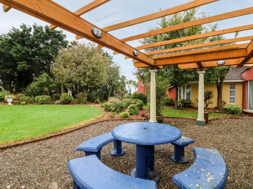 a blue table and two benches under a wooden pergola at Ballysheen House in Rosslare