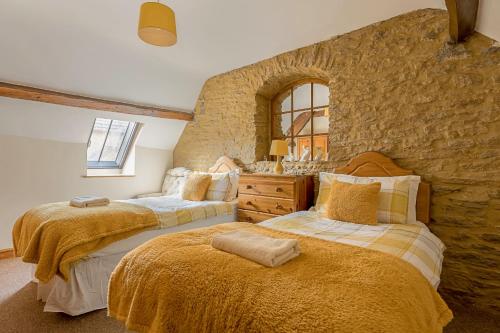 two beds in a room with a stone wall at Finest Retreats - Fives Court Cottage in North Cheriton