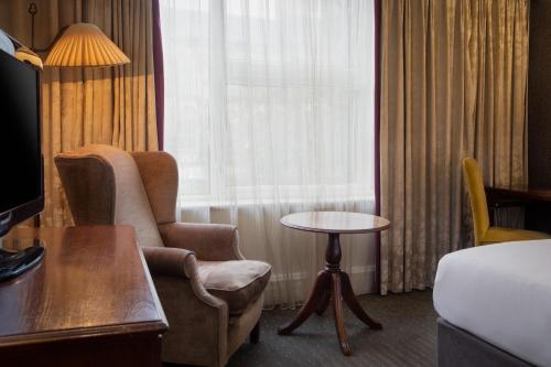 a hotel room with a chair and a table and a bed at Winchester Wessex Hotel by Sunday in Winchester