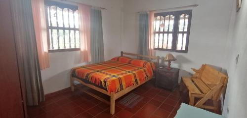 ein Schlafzimmer mit einem Bett und einem Stuhl sowie zwei Fenstern in der Unterkunft CABAÑA RURAL SANTMARTIN in Sutamarchán