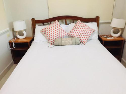 a bed with red and white pillows and two lamps at Hilamito Lodge in Tela