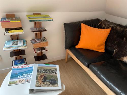 a black leather couch with an orange pillow and a book on a table at Ollediek in Houwerzijl